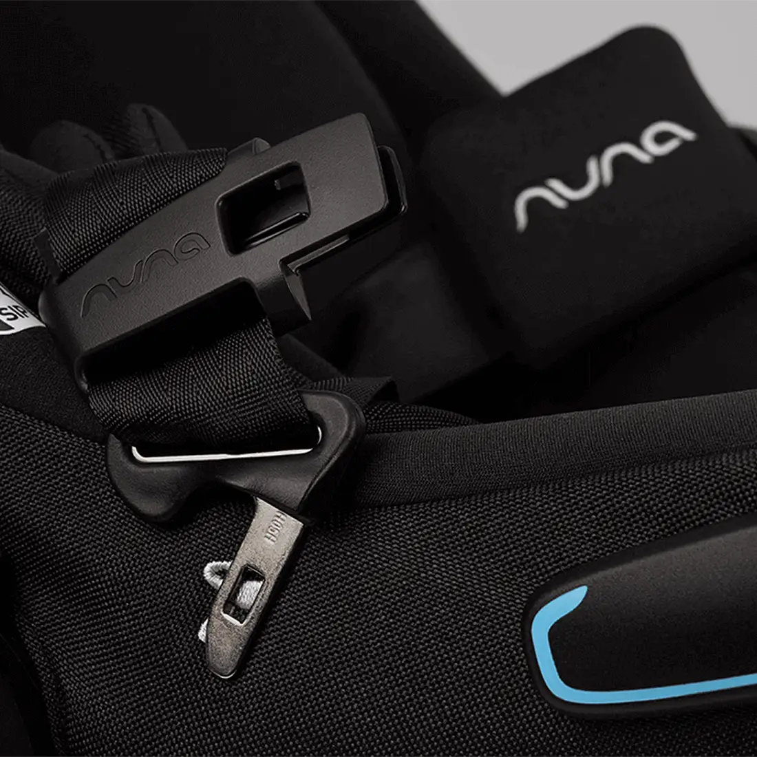 A close-up of the integrated magnetic buckle holders and harness straps on a black MIXX Next + Pipa Aire RX Travel System by Nuna car seat.