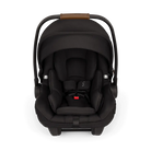 A front view of a black MIXX Next + Pipa Aire RX Travel System by Nuna infant car seat featuring a brown leatherette carry handle and safety harness straps with magnetic buckle holders, set against a checkered transparent background.