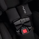 Nuna car seat with black straps and red buckle on a dark background