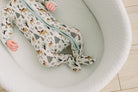 A baby wearing a long-sleeve zip-up sleep sack with a woodland animal print, lying inside a white bassinet.