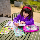 Child coloring at a table outdoors with art supplies