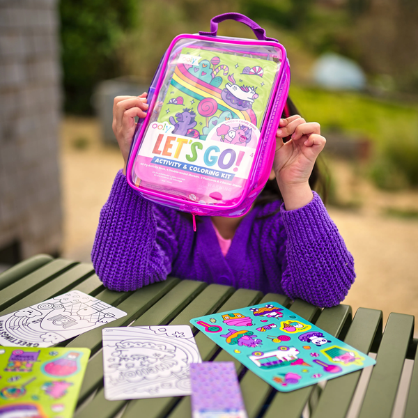 Person holding a 'Let's Go!' activity and coloring kit on a table with coloring sheets and stickers.