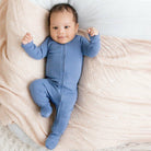 Baby in a blue onesie lying on a soft beige blanket