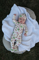Baby in floral onesie and hat lying on a white blanket outdoors