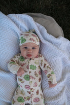 Baby in floral outfit and hat lying on a textured blanket outdoors