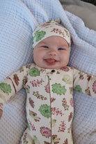 Baby wearing a floral outfit and hat, lying on a textured blanket