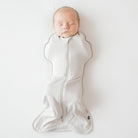 Newborn baby sleeping in a white swaddle on a light gray background