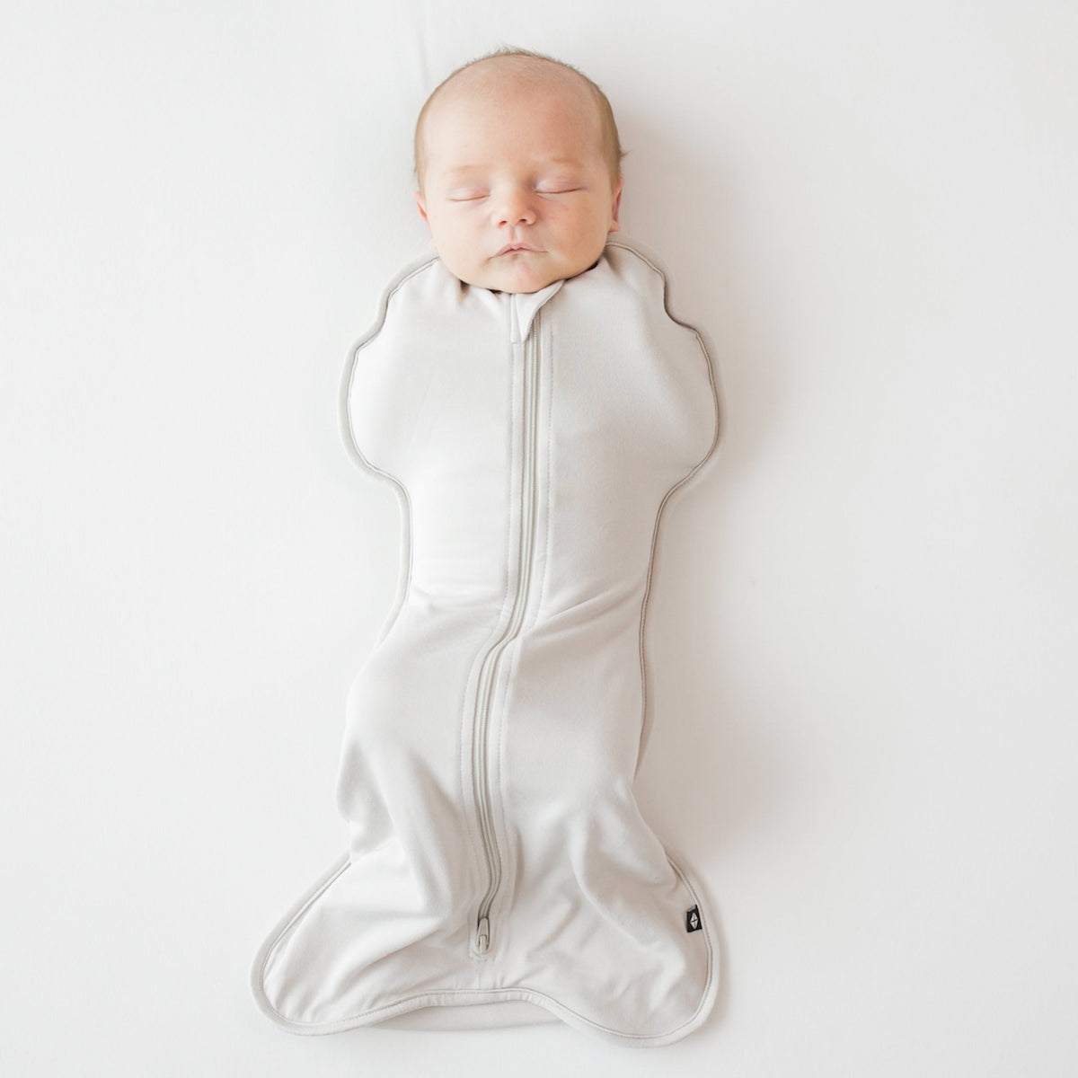 Newborn baby sleeping in a white swaddle on a light gray background