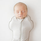Newborn baby sleeping in a light gray swaddle on a white background