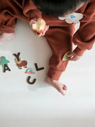 Child in brown outfit holding an apple with colorful letters on a white floor