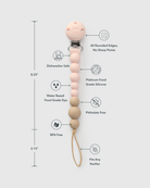 A silicone pacifier clip with a beaded handle, shown with dimension lines and feature callouts. The clip is silver metal, and the handle features a light pink top bead, pale pink beads, natural wood beads, and a tan loop.