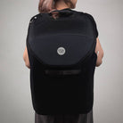 Person wearing a black backpack with a visible brand logo on a plain background