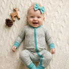 Baby in a gray and blue onesie with a bow headband, surrounded by toys on a textured surface.
