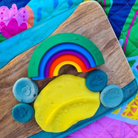 Colorful rainbow-shaped play dough on a wooden board with a colorful background