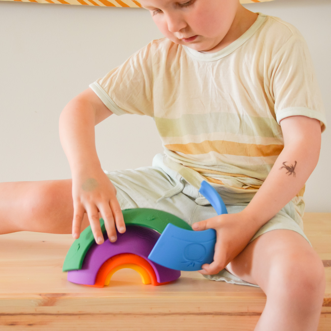 Child playing with a colorful rainbow-shaped toy on a wooden surface.