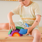 Child playing with a colorful rainbow-shaped toy on a wooden surface.