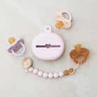 Baby pacifier with a pink case and a beaded strap on a light background