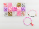 Princess Party DIY Bracelet Kit featuring a compartment storage box filled with colorful beads, alphabet letter beads, and charms next to two completed pink, purple, and gold beaded bracelets, including one spelling "PRINCESS" with a small crown and tassel charm.