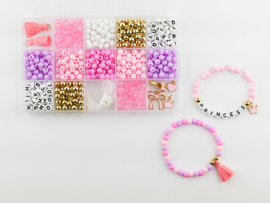 Princess Party DIY Bracelet Kit featuring a compartment storage box filled with colorful beads, alphabet letter beads, and charms next to two completed pink, purple, and gold beaded bracelets, including one spelling "PRINCESS" with a small crown and tassel charm.