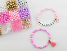 Princess Party DIY Bracelet Kit featuring a compartment storage box filled with colorful beads, alphabet letter beads, and charms next to two completed pink, purple, and gold beaded bracelets, including one spelling "PRINCESS" with a small crown and tassel charm.