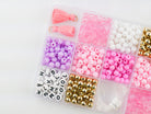 Princess Party DIY Bracelet Kit storage box shown from above, filled with sorted compartments of pink tassels, white and pink round beads, gold spacer beads, alphabet letter beads, and elastic cording.