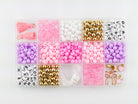 Princess Party DIY Bracelet Kit storage box shown from above, filled with sorted compartments of pink tassels, white and pink round beads, gold spacer beads, alphabet letter beads, and elastic cording.