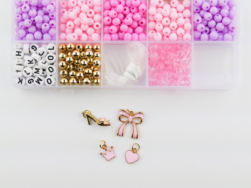 Princess Party DIY Bracelet Kit featuring an open compartment storage box filled with colorful pink, purple, and white round beads, alphabet letter beads, and gold spacer beads, alongside several gold charms including a high heel shoe, bow, crown, and heart.