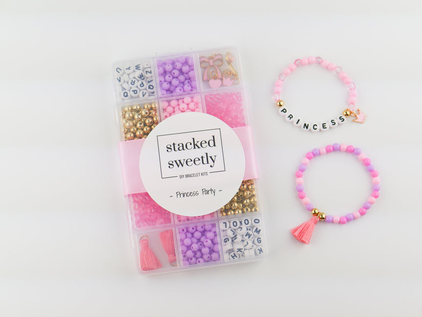Princess Party DIY Bracelet Kit featuring a compartment storage box with a "stacked sweetly - Princess Party" label, filled with colorful beads, alphabet letter beads, and charms next to two completed pink, purple, and gold beaded bracelets, including one spelling "PRINCESS" with a small crown and tassel charm.