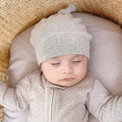 Baby in a beige outfit and hat lying on a cushion