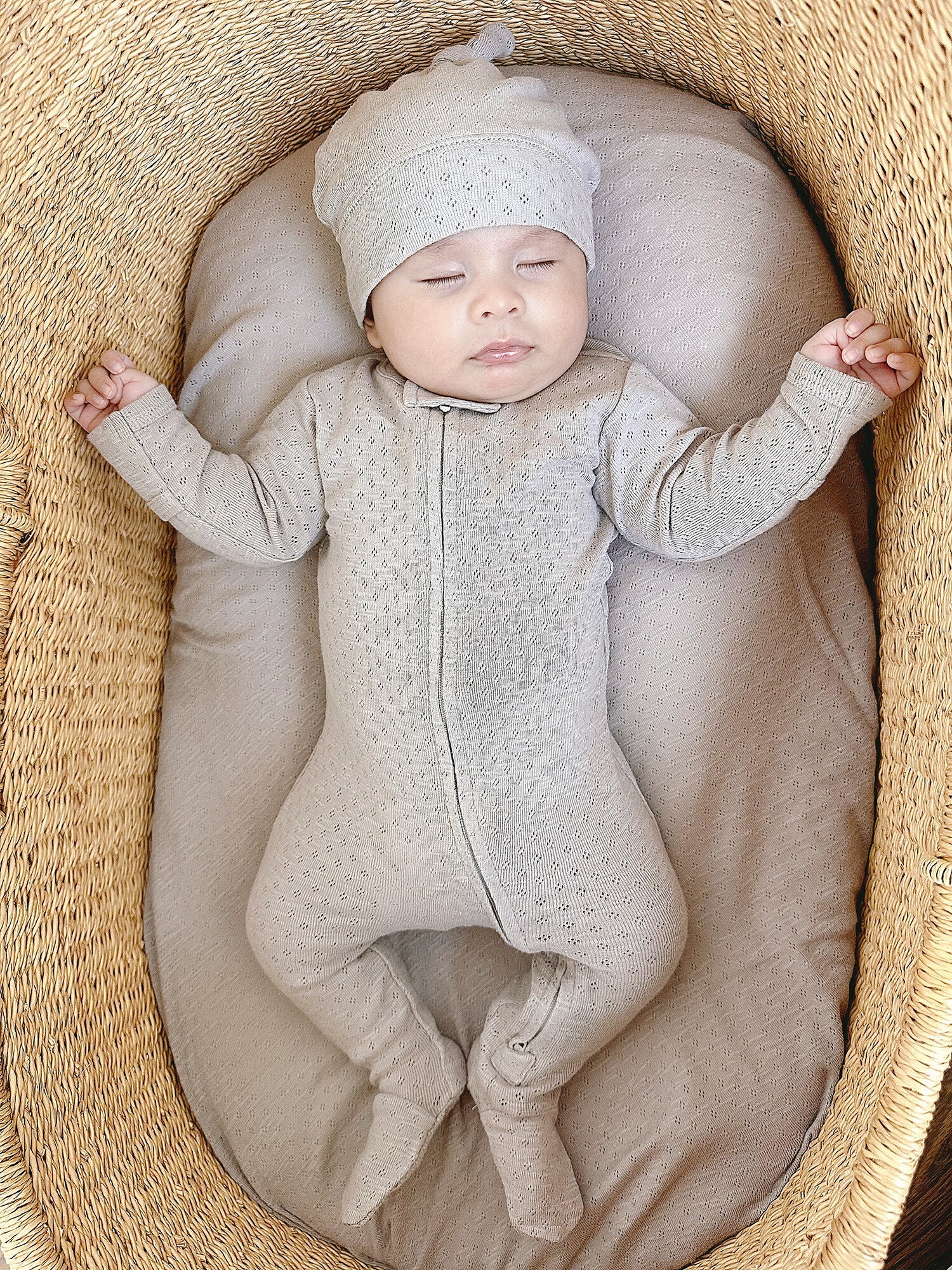 Baby in a textured outfit and hat lying on a soft surface