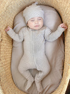 Baby in a textured outfit and hat lying on a soft surface