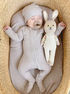 Baby in a textured outfit lying next to a plush toy in a woven basket