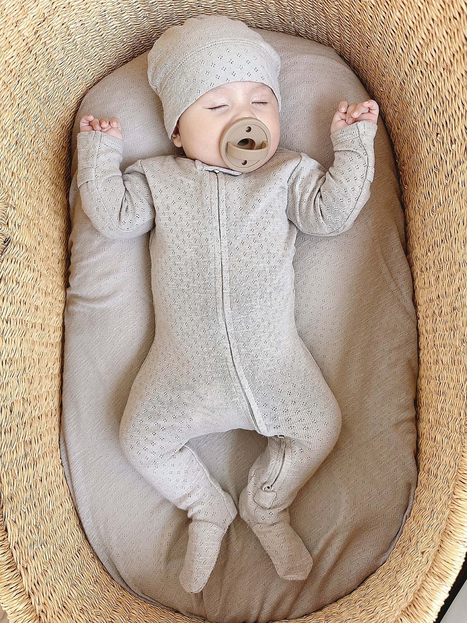 Baby in a textured outfit and hat lying in a woven basket