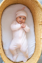 Baby in a pink outfit and hat lying in a woven basket with white bedding.