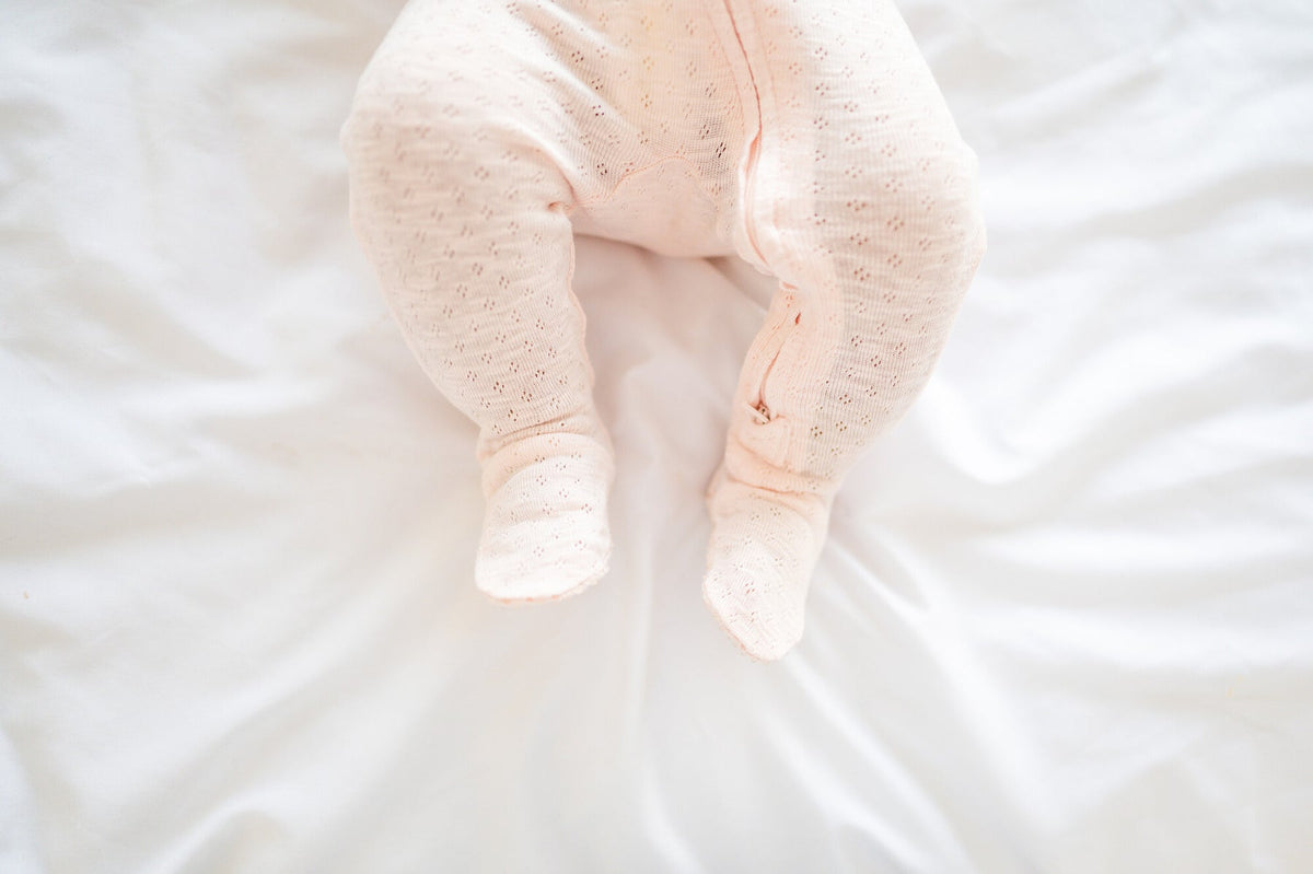 Baby legs in pink pants on a white blanket