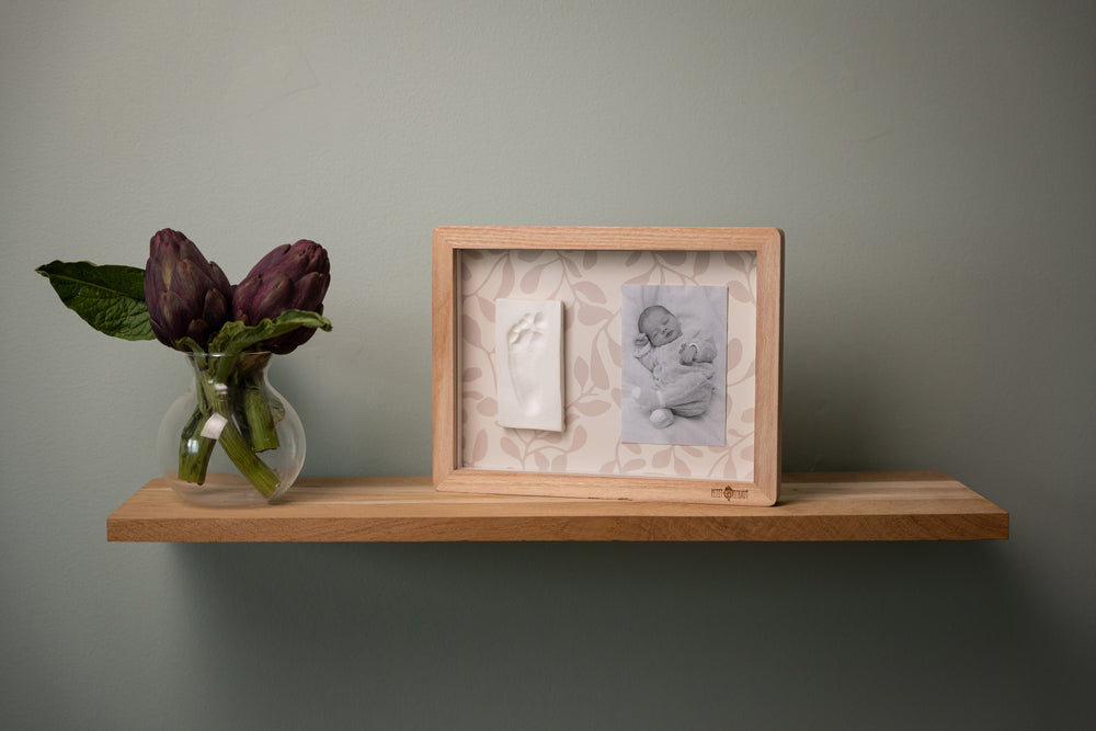 Wooden shelf with decorative items including a vase with purple flowers and framed artwork against a plain wall.