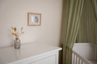 Nursery room with white dresser, crib, and framed picture on wall.