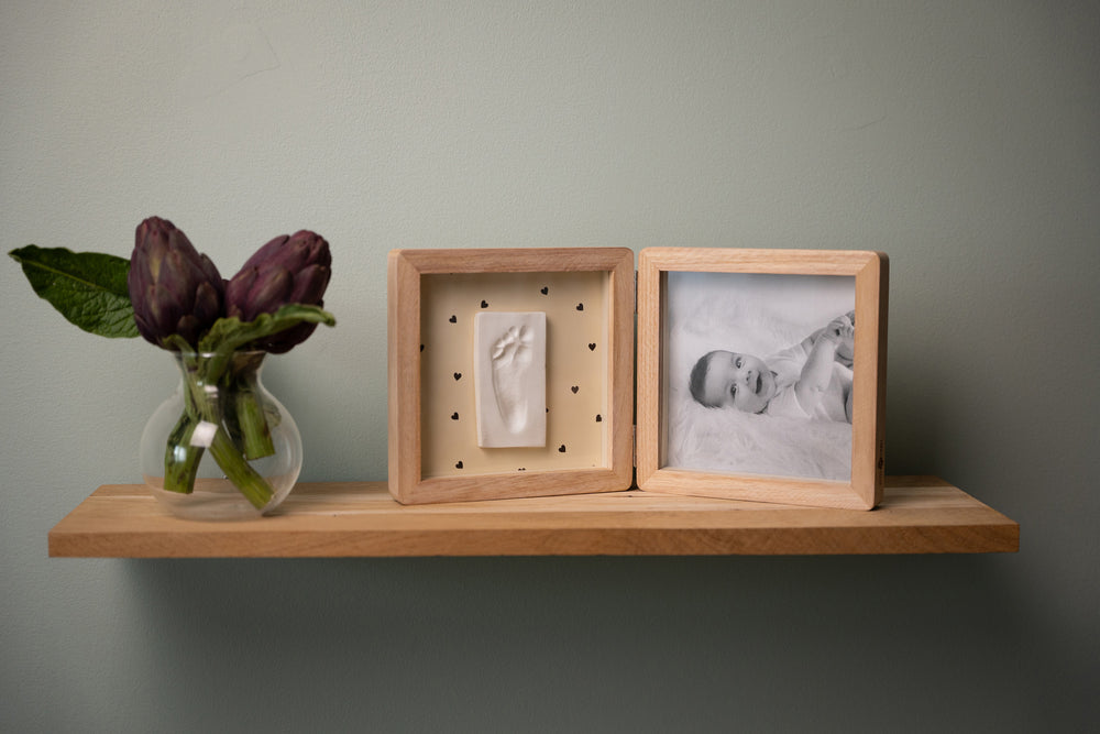 Wooden shelf with a vase of purple flowers and two wooden frames on a plain wall.