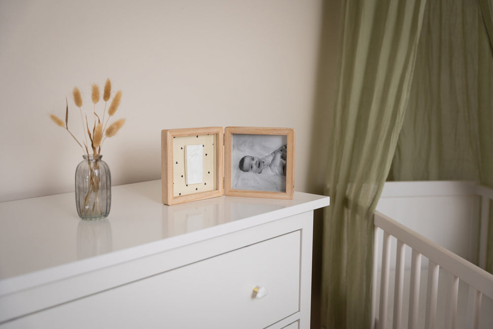 White dresser with framed photos and a vase of dried plants next to a crib.