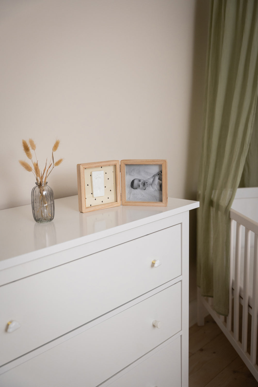 White dresser with decorative items and a crib in a room.