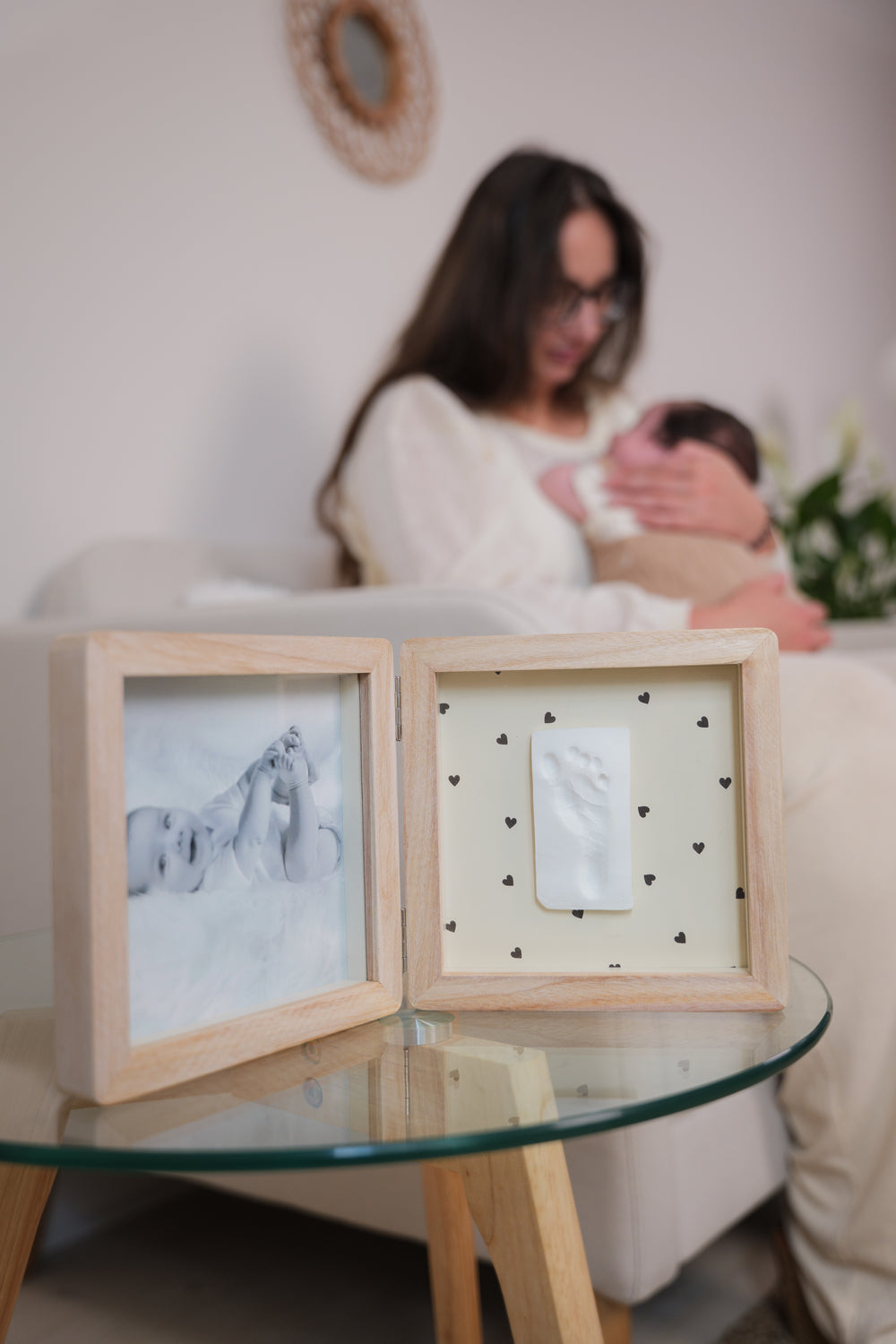 Woman holding a baby with two framed artworks on a glass table.