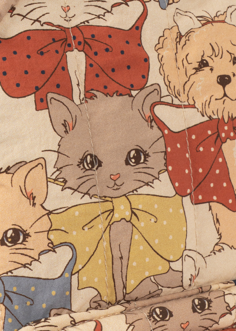 Close-up of a vintage-style printed fabric or wallpaper featuring illustrated cats and dogs wearing red polka-dot bows, with a cream background and warm vintage tones.