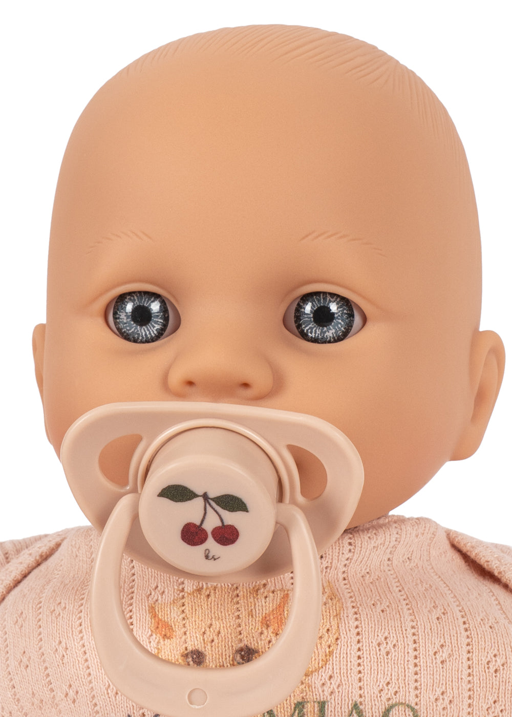 A close-up of a baby doll with a realistic bald head, large blue-gray eyes, a pacifier with a cherry design, and a pale pink knit outfit on a white background.