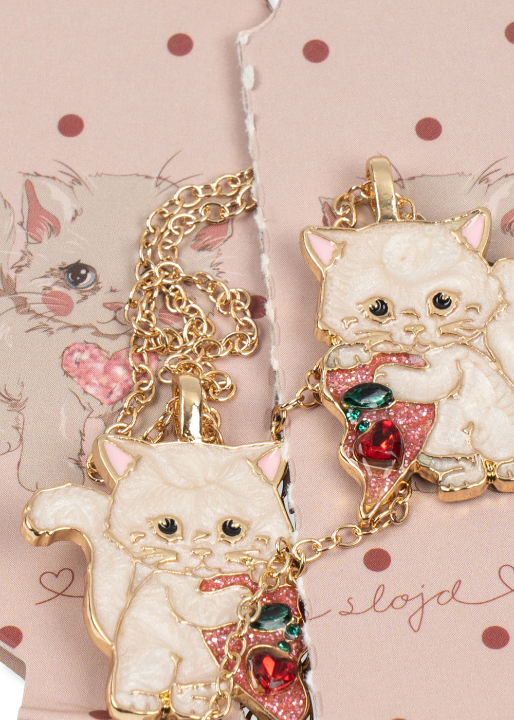 A close-up of a gold-tone pendant necklace featuring a cute white cat holding a slice of pizza with red and green toppings, displayed on a pink polka-dot card.
