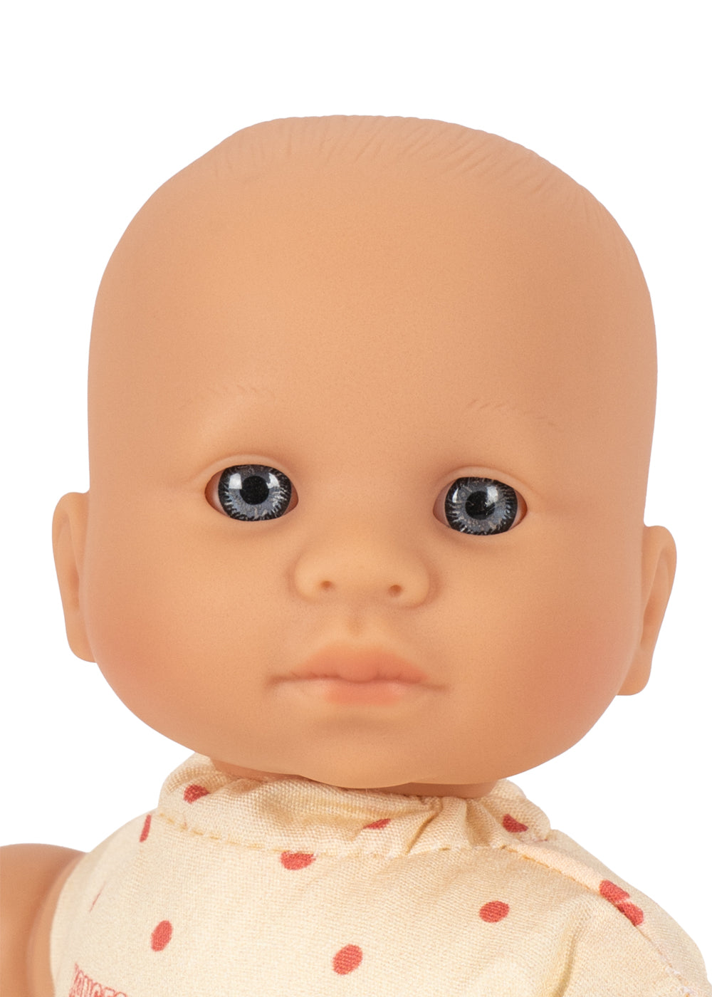 Close-up of a baby doll with a bald head, realistic skin tone, blue-gray eyes, and a cream-colored top with red polka dots, shown against a plain white background.