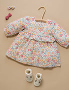 Floral dress on a hanger with baby shoes and hair clips on a beige background