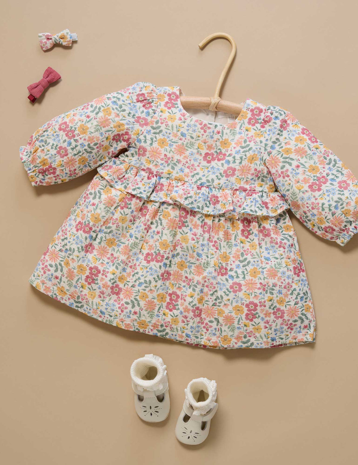 Floral dress on a hanger with baby shoes and hair clips on a beige background
