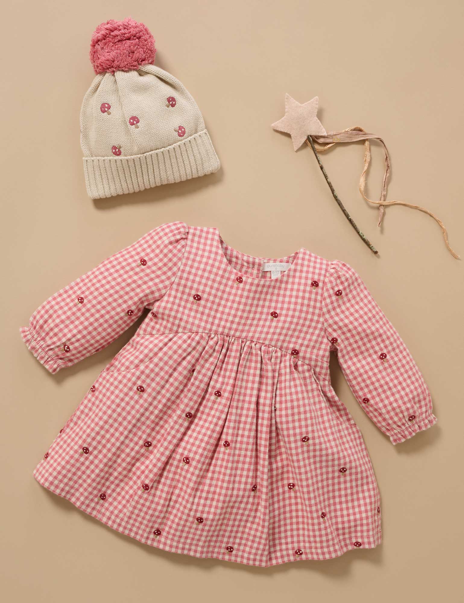 Pink checkered dress with floral details, matching hat, and wand on a beige background