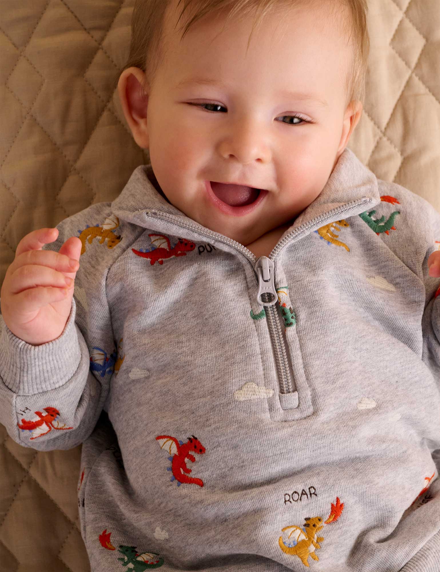 Baby wearing a gray sweater with animal prints on a beige blanket
