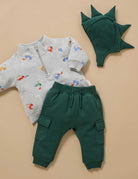Children's outfit with gray zip-up hoodie, green cargo pants, and dinosaur hat on a beige background